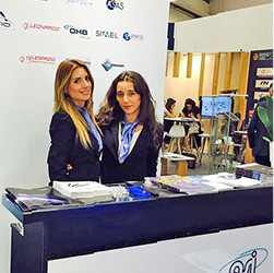 Hostesses at the reception desk of a B2B trade fair booth featuring Leonardo, DHB, Simel and Telepromo &mdash; event staff in New York