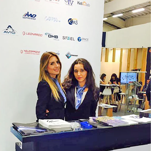 Hostesses at the reception desk of a B2B trade fair booth featuring Leonardo, DHB, Simel and Telepromo &mdash; event staff in New York